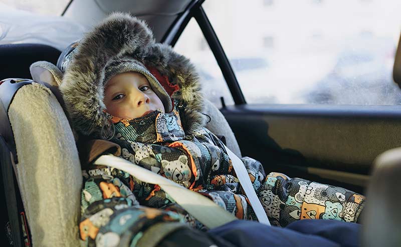 boy in heavy coat rides in carseat