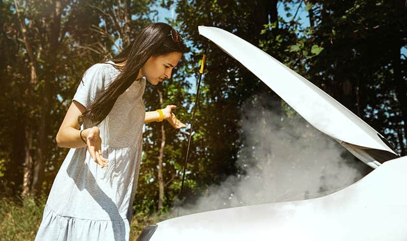 woman stares in confusion at smoking car engine
